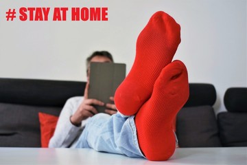 Close-up view of an homebound men's socks lying on a sofa with his feet on a table while reads on...