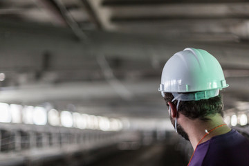 Worker in white helmet looks at blurred dirty dusty workshop. Void concept, gray background, copy...