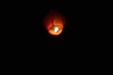 Fototapeta na wymiar A red coloured sky lantern with the flames showing clearly lifiting off