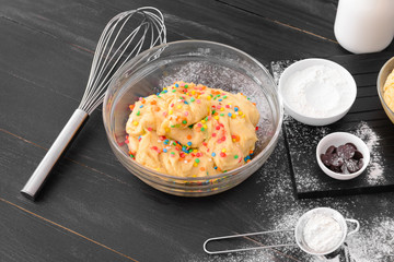 Bowl with sweet dough and products on table