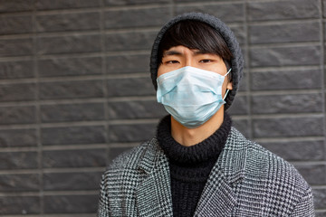 Portrait of asian young man . Chinese guy in facial mask against 2019-nCov looks upset and miserable . Outside. Grey background. Pandemic disease. Virus protection. Chinese coronavirus outbreak.