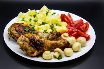 Tasty cooked chicken legs with potatoes, tomatoes, mushrooms on a white plate. Delicious potatoes with onion and dill on dinner, lunch. Amazing chicken legs cooked in spice. Ukrainian healthy meal