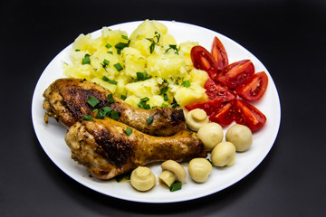 Tasty cooked chicken legs with potatoes, tomatoes, mushrooms on a white plate. Delicious potatoes with onion and dill on dinner, lunch. Amazing chicken legs cooked in spice. Ukrainian healthy meal