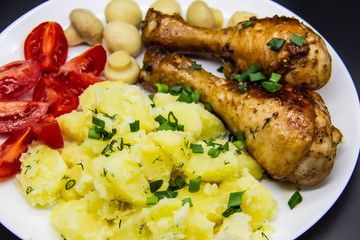 Tasty cooked chicken legs with potatoes, tomatoes, mushrooms on a white plate. Delicious potatoes with onion and dill on dinner, lunch. Amazing chicken legs cooked in spice. Ukrainian healthy meal