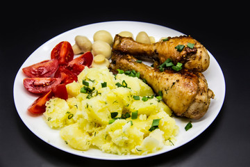 Tasty cooked chicken legs with potatoes, tomatoes, mushrooms on a white plate. Delicious potatoes with onion and dill on dinner, lunch. Amazing chicken legs cooked in spice. Ukrainian healthy meal