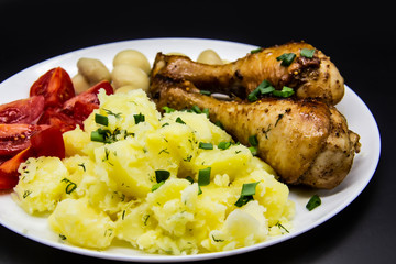Tasty cooked chicken legs with potatoes, tomatoes, mushrooms on a white plate. Delicious potatoes with onion and dill on dinner, lunch. Amazing chicken legs cooked in spice. Ukrainian healthy meal