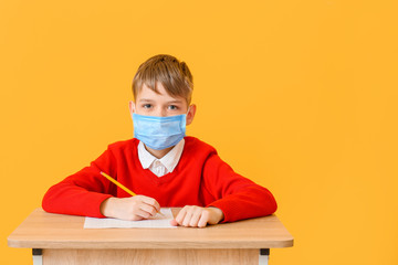 Pupil in medical mask passing exam against color background. Concept of epidemic