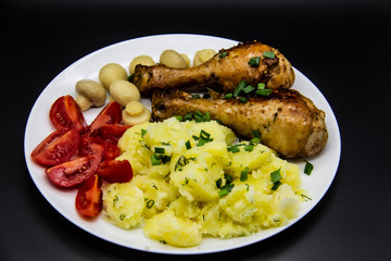 Tasty cooked chicken legs with potatoes, tomatoes, mushrooms on a white plate. Delicious potatoes with onion and dill on dinner, lunch. Amazing chicken legs cooked in spice. Ukrainian healthy meal