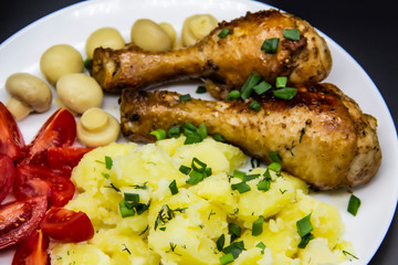 Tasty cooked chicken legs with potatoes, tomatoes, mushrooms on a white plate. Delicious potatoes with onion and dill on dinner, lunch. Amazing chicken legs cooked in spice. Ukrainian healthy meal