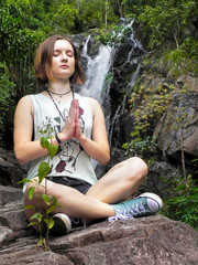 Young woman in yoga lotus position sitting near a waterfall