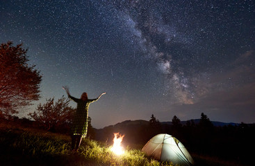 Amazing starry night in the mountains, girl is standing with her hands up and looking at Milky Way...