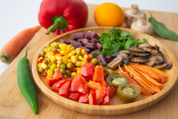 Nutritious and healthy buddha fajita bowl with sweet corn, green peas, red bell pepper, jalapenos, carrots, mushrooms, spinach, beetroot and sweet potatoes surrounded by ingredients and lemon
