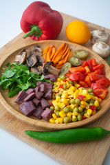 Nutritious and healthy buddha fajita bowl with sweet corn, green peas, red bell pepper, jalapenos, carrots, mushrooms, spinach, beetroot and sweet potatoes surrounded by ingredients and lemon
