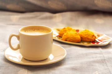 cup of morning coffee and cookies in bed. a cup of coffee on a saucer and cookies on a stand on the bed in the morning sun. morning awakening. morning breakfast in bed