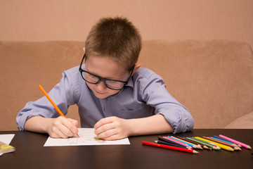 boy draws while sitting at a black table. The kid draws with colored pencils.