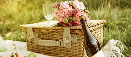 Picnic basket with flowers, glass and vine on the grass backgrou