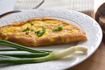 Fluffy breakfast omelette with green spring onions and fresh toast bread on a wooden surface with a napkin and metal fork
