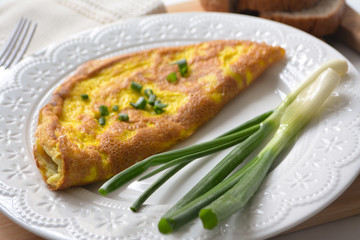 Fluffy breakfast omelette with green spring onions and fresh toast bread on a wooden surface with a napkin and metal fork