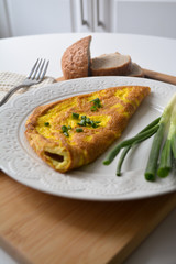 Fluffy breakfast omelette with green spring onions and fresh toast bread on a wooden surface with a napkin and metal fork