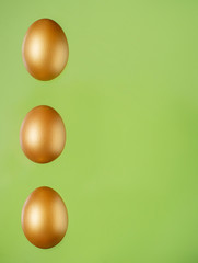Row of three golden eggs on light green background