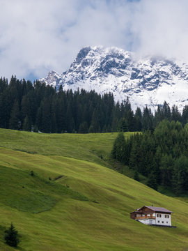 Fresh snow on the summit of Karhorn, green alpine pastures and an isolated house in Lech, Vorarlberg, Austria