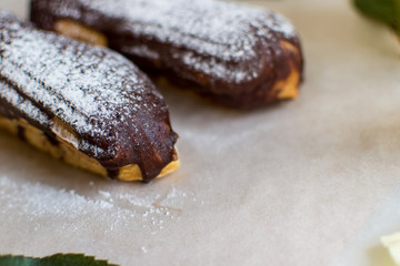 French eclairs with custard sprinkled with powdered sugar and white roses, petals, green leaves on light background