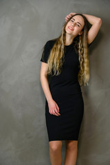 Vertical photo of a cute caucasian teenager girl in a black dress with long hair in the studio on a gray background