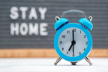 analog alarm clock on the background of English text stay at home on a gray felt Board. concept of...