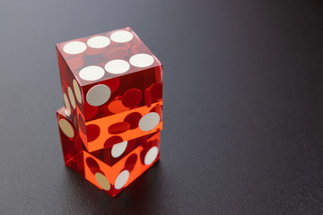 Two red glass dice on a black matte background with side lighting. Dice on the other, on top six.
