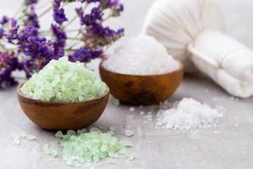 Sea salt in bowl, aroma oil in bottles, Wellness and flowers on grey textured background and...