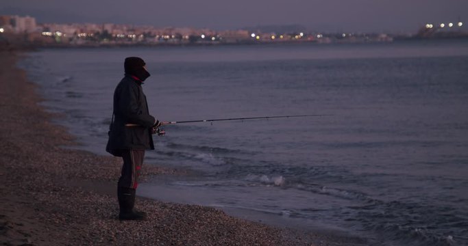 Wide shot shoreline at dawn, male fisherman surf fishing Mojacar, Almeria, Spain