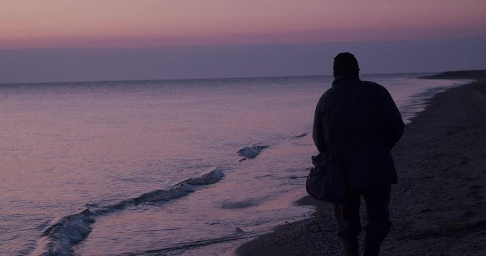 Real time full body shot fisherman walking beach sunrise, Mojacar, Almeria, Spain