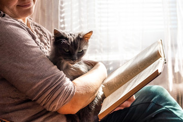 Elderly woman reading a book while holding a cat_