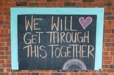Chalk sign saying we will get through this together on a brick wall.  Written during the Coronavirus pandemic lockdown.