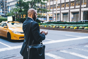 Black worker typing message while crossing road