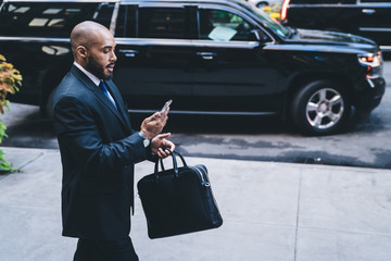 Black businessman walking with briefcase and using smartphone
