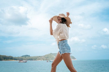 Fototapeta na wymiar Beautiful young happy slender woman with long curly hair and a beautiful smile in a straw hat on walks against the background of the turquoise tropical sea at the resort, travel and lifestyle concept