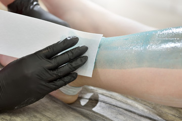 The process of female waxing. Beautician removes wax with hair from female legs.