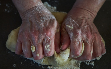 woman making bread with their hands in the kitchen on a dark backround. 