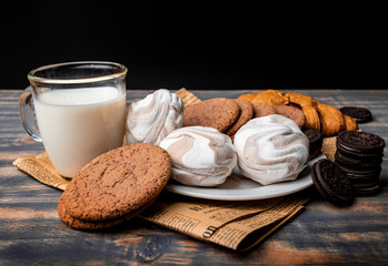 Milk with cookies, marshmallows and pastries on newsprint on a black background