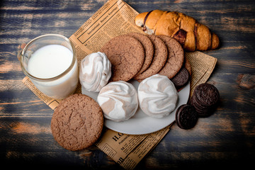 Milk with cookies, marshmallows and pastries on newsprint on a black background