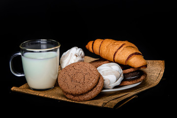 Milk with cookies, marshmallows and pastries on newsprint on a black background