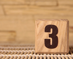 Wooden cube with the number three on a beige background.