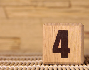 Wooden cube with the number four on a beige background.