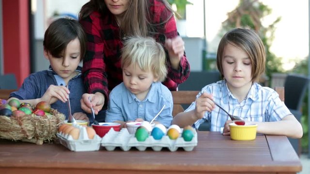 Sweet children, brothers, coloring and paiting eggs for Easter in garden, outdoor at home in backyard