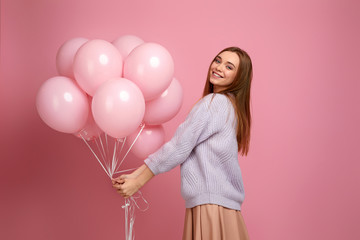 Smiling carefree girl posing with pastel pink air balloons isolated over pink background. Beautiful happy young woman on a birthday holiday. space for text