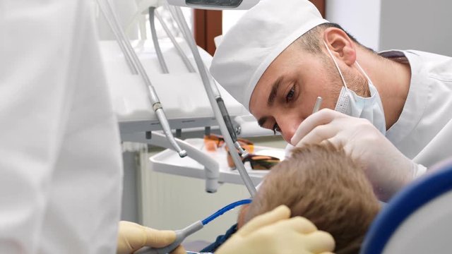 Confident male dentist in uniform treating teeth to child boy. Close up shot on 4k RED camera