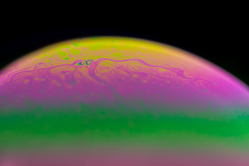 Psychedelic abstract planet from soap bubble, Light refraction on a soap bubble, Macro Close Up in soap bubble. Rainbow colors on a black background. Model of Space or planets universe cosmic galaxy.