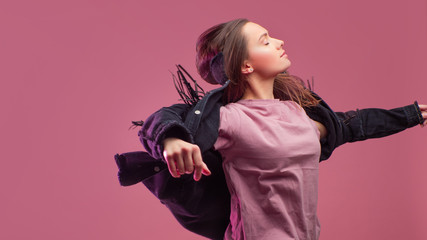 cheerful girl in a fringed jacket dances on a pink background.