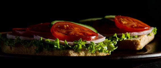 delicious sandwiches with ham, lettuce, cucumber and tomato on a dark background